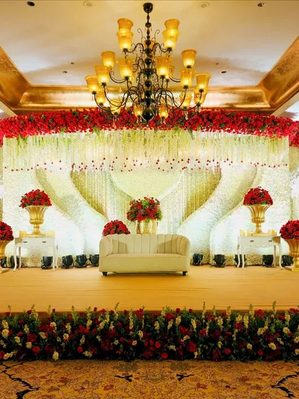 A closer view of the magnificent red and white reception stage, showcasing the dense floral work and the heart-shaped draping of flower strings.
