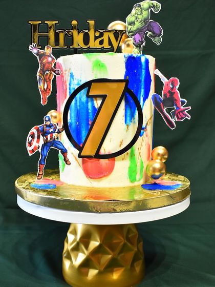 A superhero-themed cake for a 7th birthday, featuring Avengers characters like Iron Man, Hulk, Captain America, and Spider-Man against a colorful, paint-splatter background.