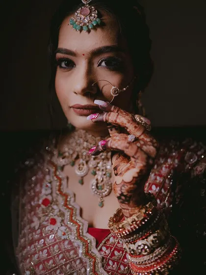 A powerful portrait of the bride looking directly at the camera, her hand gently touching her face, showcasing her bold makeup and jewelry.