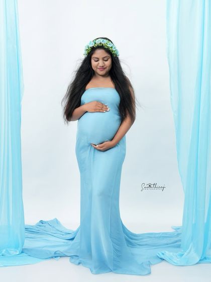 A solo portrait of a mother-to-be in a light blue wrap gown, framed by matching drapes. The monochromatic color scheme creates a serene and artistic look.