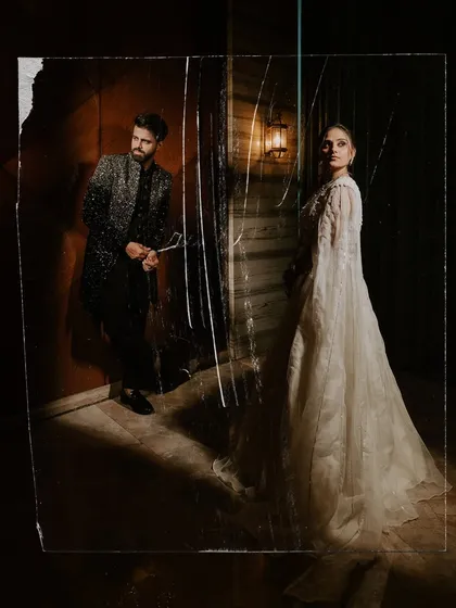 A full-length couple portrait with a creative, distressed foreground effect, adding a raw and artistic feel to their Sangeet look.