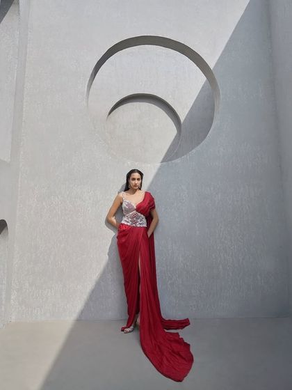 A tale of contrasts. This crimson pre-draped sari flows like liquid fire, while the hand-embellished pearl corset belt cinches the silhouette with regal restraint.
