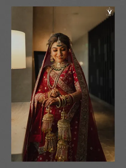 A classic bridal portrait showing the bride in her stunning red lehenga, holding her kaleeras. The soft lighting and her gentle smile create an image of timeless grace and beauty.