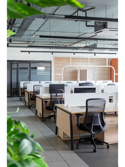 A perspective of the workstation rows, viewed through lush indoor plants. This biophilic design approach helps to soften the corporate environment and improve the overall well-being of the employees.