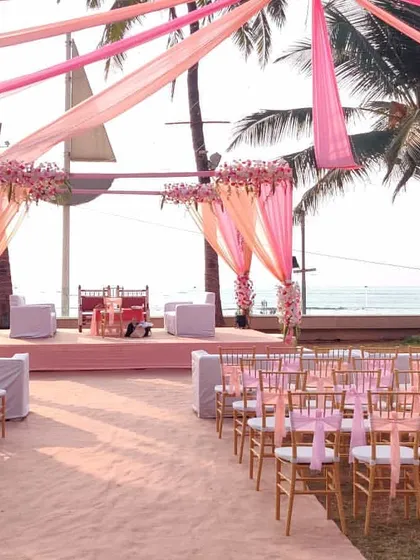 A view down the aisle towards a stunning pink-themed mandap. The flowing drapes from the canopy overhead lead the eye directly to the main ceremony area, creating a sense of grandeur.
