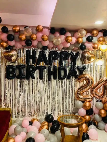 A classic birthday backdrop with a silver fringe curtain and a balloon arrangement in rose gold, black, and grey for a 24th birthday.