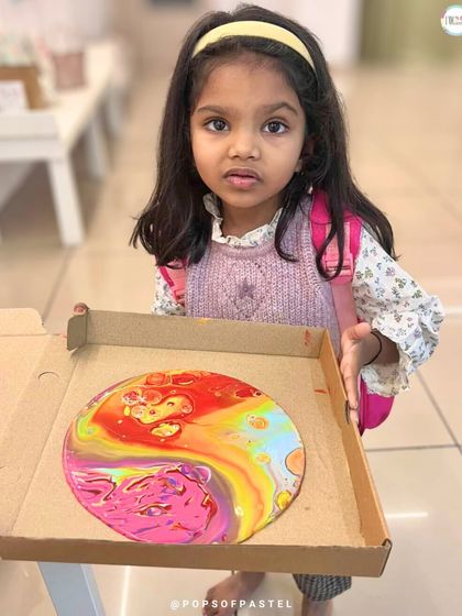A little girl carefully carries her freshly made fluid art piece in a pizza box, a clever and safe way to transport wet art home.