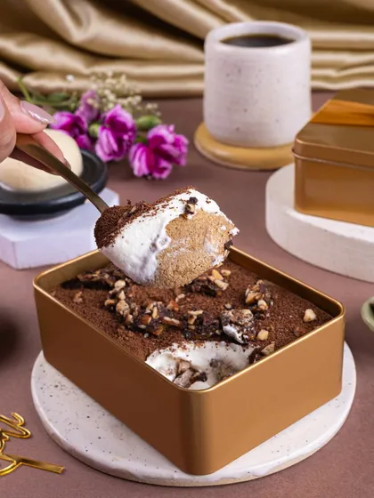 A close-up of a spoon scooping into a Rasgulla Tiramisu. This shot captures the soft texture and different layers of the fusion dessert, making it look incredibly tempting.