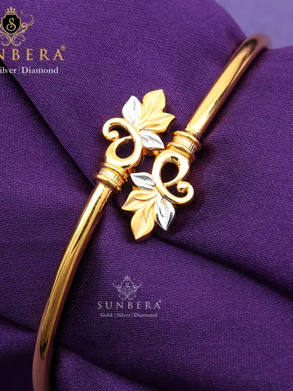 A stylish gold open-cuff bracelet featuring two-tone leaf motifs. The combination of yellow and white gold adds a contemporary touch to this nature-inspired design.