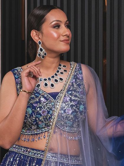 A model wearing a royal blue lehenga with intricate floral embroidery. The matching jewellery set is also available for rent.