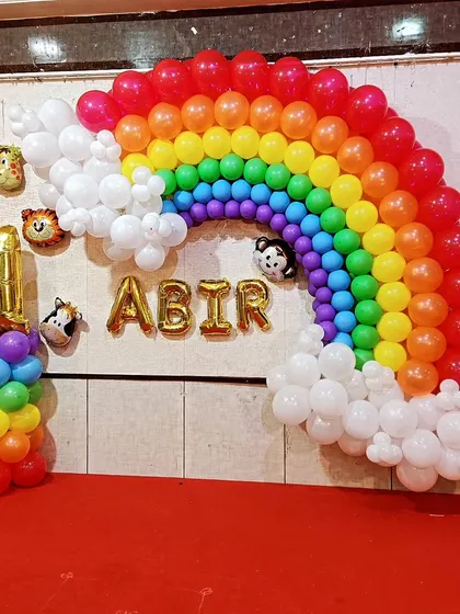 A vibrant rainbow balloon arch created for a first birthday party. This wall decoration includes white balloon clouds, animal head foil balloons, and a gold foil name and number, making for a cheerful photo backdrop.