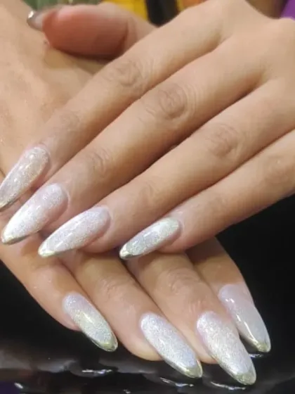 A glamorous French manicure with silver glitter tips on long, stiletto-shaped nails.