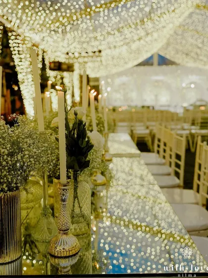 A long dining table set for the sangeet feast, with candles and flowers reflected in the mirrored surface. The repetition of lights creates a stunning visual corridor.