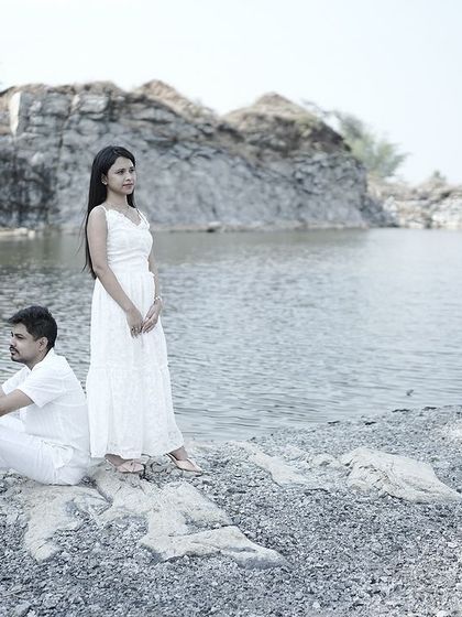 A wide shot of a couple by a quarry lake, dressed in white, creating a serene and peaceful pre-wedding portrait.