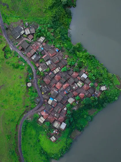 A top-down view of a small village on the banks of the Kondeshwar lake. The red-tiled roofs create a beautiful pattern against the green landscape.