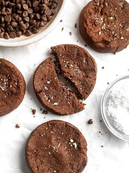 A minimalist, top-down shot of broken chocolate cookies. The clean white background and simple composition put all the focus on the crumbly texture and rich chocolate color.