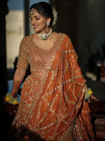 A candid shot of a client looking beautiful in the burnt orange gota pati lehenga. The intricate embroidery and rich color make it a perfect choice for a mehendi or wedding ceremony.