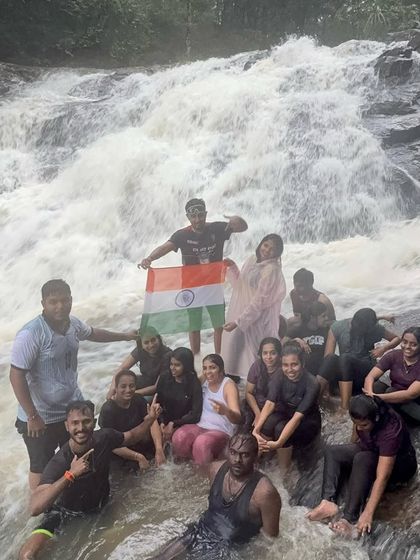 Celebrating the spirit of India with the national flag at the base of a powerful waterfall during a monsoon trek.