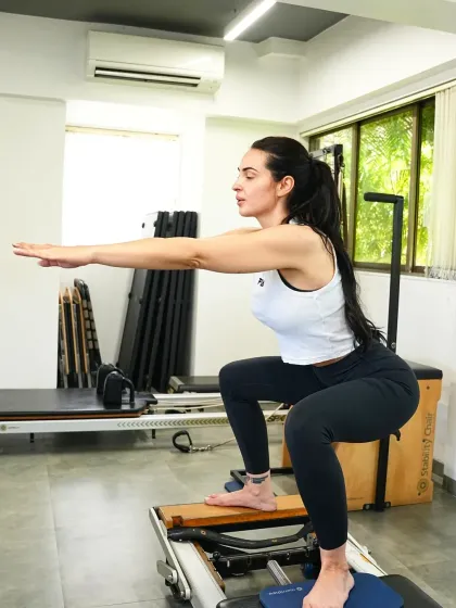 A client performs a deep squat on the reformer's jumpboard. This exercise builds lower body strength and power in a controlled, joint-friendly way.