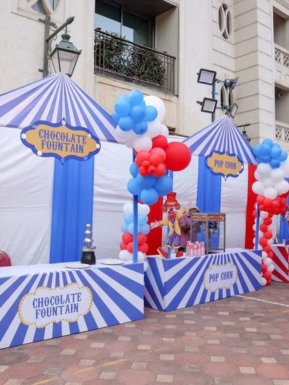 Classic carnival food stalls, like this one for a chocolate fountain and popcorn, are designed with striped awnings and balloon decor to perfectly match the overall theme.