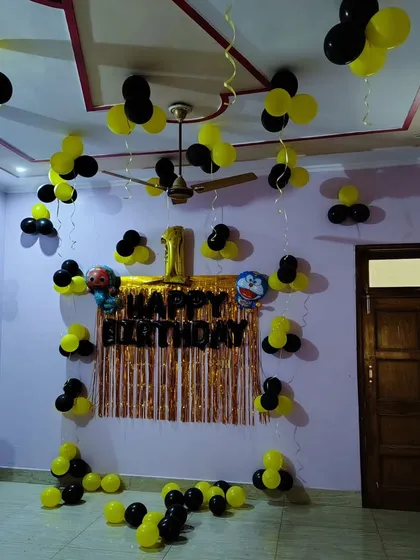 A simple home birthday decoration with black and yellow balloons, a foil curtain backdrop, and character balloons.
