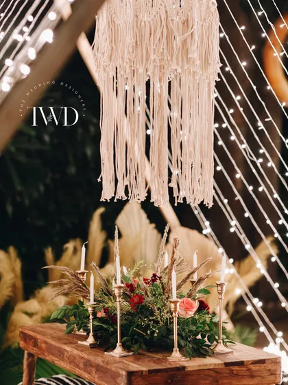 A close-up of the boho decor, featuring a large macrame chandelier, wooden furniture, and brass candlesticks. The look is earthy, elegant, and romantic.