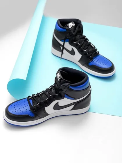 These blue and black Nike high-tops are styled with a curved piece of blue paper, adding a simple graphic element. The clean composition and bright lighting highlight the shoe's iconic silhouette.