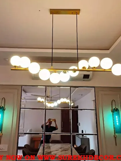 A well chosen chandelier can define a dining space. Here, a modern 11 ball fixture in a golden finish hangs above the dining table, its light beautifully reflected in the custom gridded mirror wall, which also helps to make the space feel larger and more dramatic.
