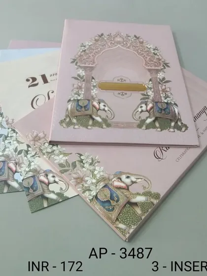 A blush pink invitation featuring two elephants under a floral arch. The design is sweet and traditional, with three inserts to accommodate all your event details.