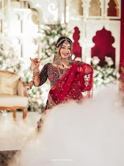 The bride, Reshma, making a grand entrance through a cloud of smoke. This dramatic shot is perfect for a cinematic wedding film opening.
