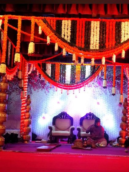 For this wedding mandap, I used pillars decorated with stacked golden pots alongside columns of marigold flowers. The canopy features orange, white, and dark green garlands for a vibrant look.