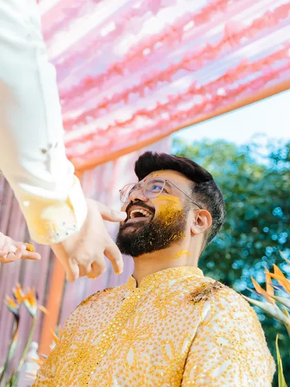 A candid, upward-looking shot of the groom laughing as turmeric is applied to his face during his Haldi ceremony at Taj Corbett.