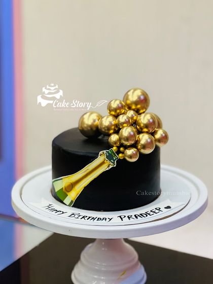 A classy and celebratory champagne bottle cake. This elegant black cake features a champagne bottle popping with golden bubbles, all completely edible.