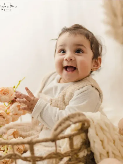 A close-up shot of a happy baby in a basket, interacting with some flowers. We use simple props to bring out their natural curiosity.