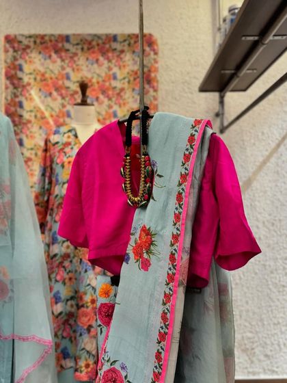 A beautiful floral print saree in pastel blue with a pink border, paired with a vibrant pink blouse for a stunning contrast.