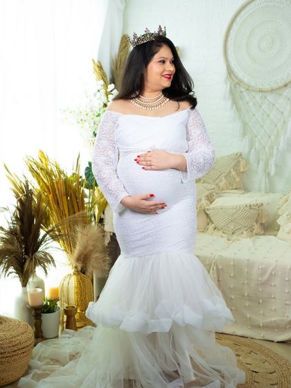 A vision in white. This elegant mermaid gown features lace sleeves and a tulle train, creating a bridal-inspired look for a timeless maternity portrait in our boho studio.