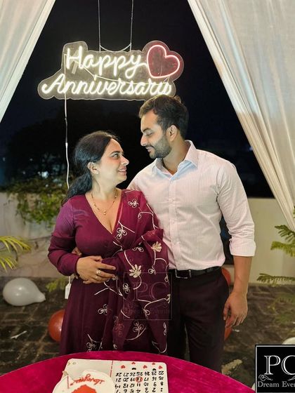 A happy couple celebrating their anniversary with our romantic terrace setup. The 'Happy Anniversary' neon sign and canopy of lights provide the perfect backdrop for their special moment.