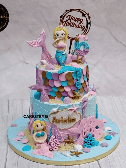 An enchanted two-tier mermaid cake for a sixth birthday. This choco-vanilla cake is decorated with shimmering mermaid scales, tails, and other sea elements in a beautiful palette of pink, purple, and teal.