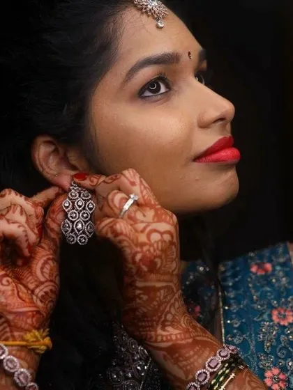 A candid shot of the bride putting on her earrings. This highlights her side profile, the soft hairstyle, and the beautiful henna that completes her reception look.