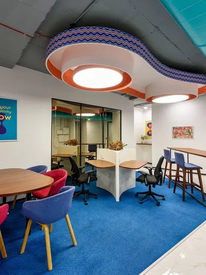 A colorful collaboration area with a custom-designed, wave-like lighting fixture overhead. The space uses a mix of table seating and high-top counters.
