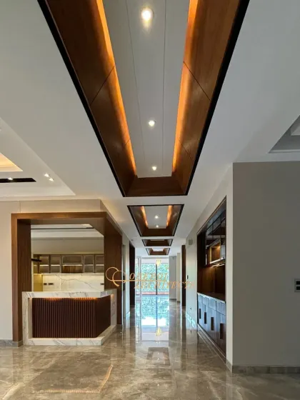 This grand corridor features a striking ceiling design with recessed wood panels and ambient lighting, guiding the eye through the space. The polished marble floor reflects the light, enhancing the sense of luxury.