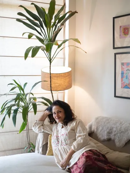 A warm and inviting portrait of a woman relaxing on her sofa at home, surrounded by plants and soft light.