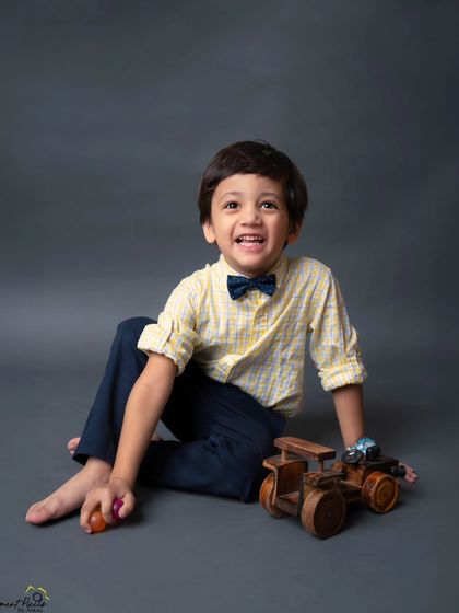 A joyful laugh and a classic bow tie. This portrait of a little boy playing with his wooden toys is a timeless capture of childhood happiness.