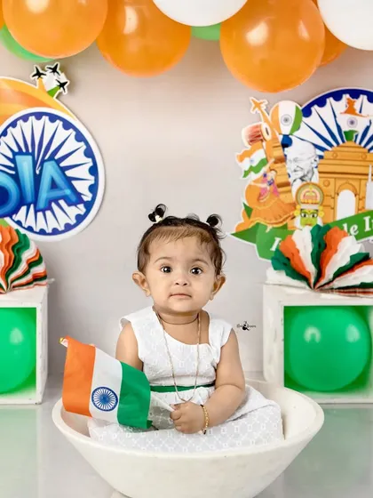 A sweet portrait of a baby girl holding the flag, with a backdrop of tricolor balloons for Independence Day.