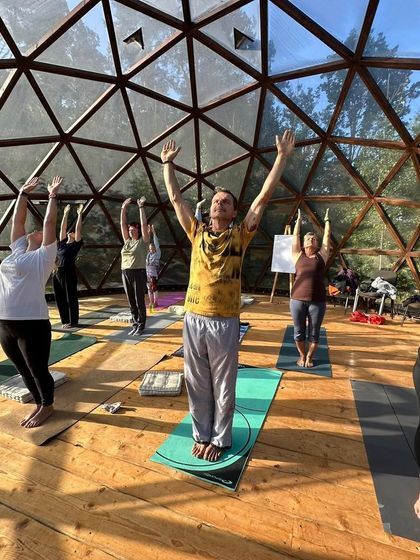 A group of students practicing a variation of Surya Namaskar (Sun Salutation) inside the beautiful geodesic dome. The natural light and wooden floors create a warm and inviting atmosphere for our yoga practice.