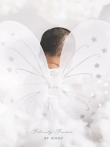 An angel has turned one! This creative shot from behind, showing her fairy wings amidst soft clouds, is a unique and beautiful way to mark a first birthday.