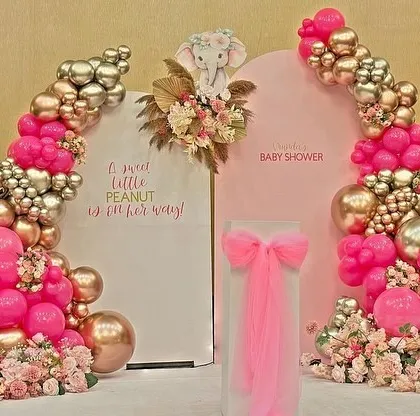 A full view of the dual-arch backdrop in pink and metallics, decorated with florals and an elephant motif for a baby girl's shower.