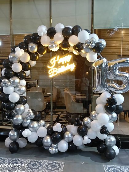 A 15th birthday party in a restaurant, with a black, white, and silver balloon ring and a neon sign.