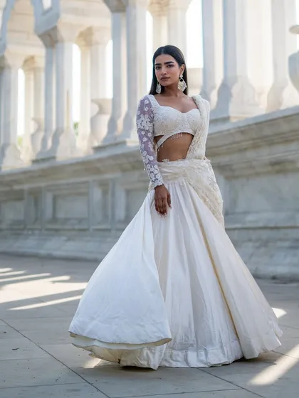 A full view of our elegant ivory lehenga with a sheer, long-sleeved embroidered blouse. The side cut-out adds a modern touch to this classic look.