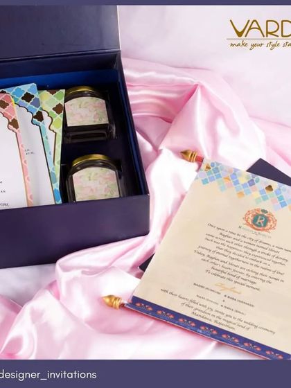 This stylish invitation box combines modern design with traditional hospitality. The box contains beautifully designed cards with geometric patterns and two jars for sweets or dry fruits, all presented on a bed of pink satin.